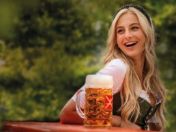 Eine junge Frau mit langen blonden Haaren sitzt im Dirndl an einem Biertisch und genießt eine Maß Bier von Fürst Wallerstein