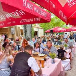 Menschen sitzen unter roten Fürst Wallerstein Sonnenschirmen im Sixengarten