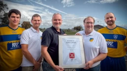 Harald Schmidt vom F&uuml;rst Wallerstein Brauhaus &uuml;berreicht Vertretern des FC Birkhausen eine Ehrenurkunde f&uuml;r 50 Jahre Partnerschaft. Zwei Fu&szlig;ballspieler in gelb-blauen Trikots begleiten die Ehrung am Sportplatz.